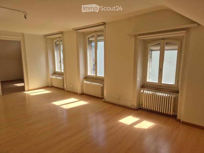 Empty room with wooden flooring, large windows with blinds, radiators, and natural light streaming in.