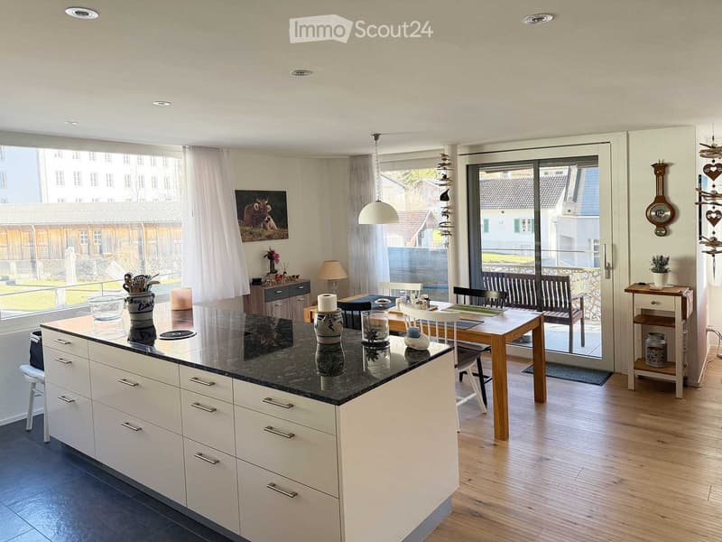 white cabinets, black marble countertop, dining table with chairs, sliding glass door leading to a balcony, large windows with a view of the outside, hanging lamp, wooden floor