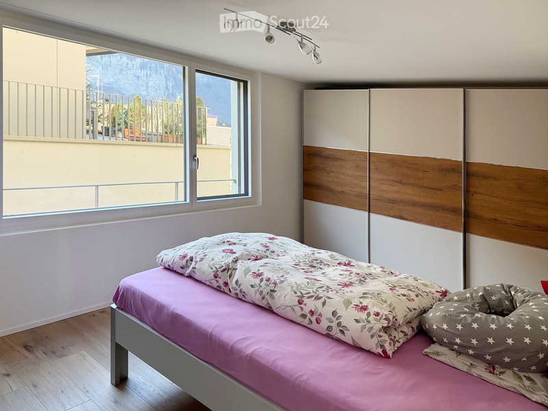 single bed, floral cover, wooden floor, large window with balcony, built-in wardrobe, track lighting