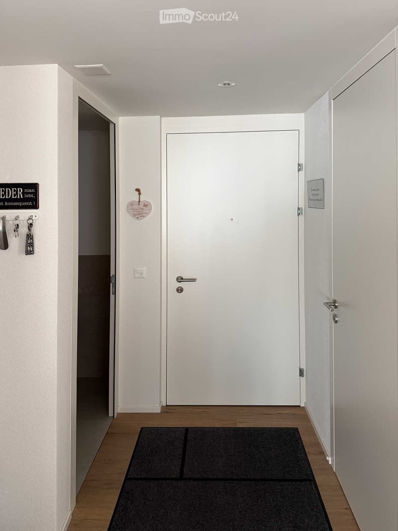modern clean entryway, white walls, wooden floor, front door, black mat, two sets of keys hanging on wall