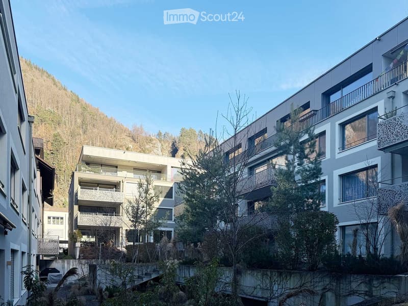 modern apartment building, grey walls, large balconies, surrounded by trees and plants, located on a hillside