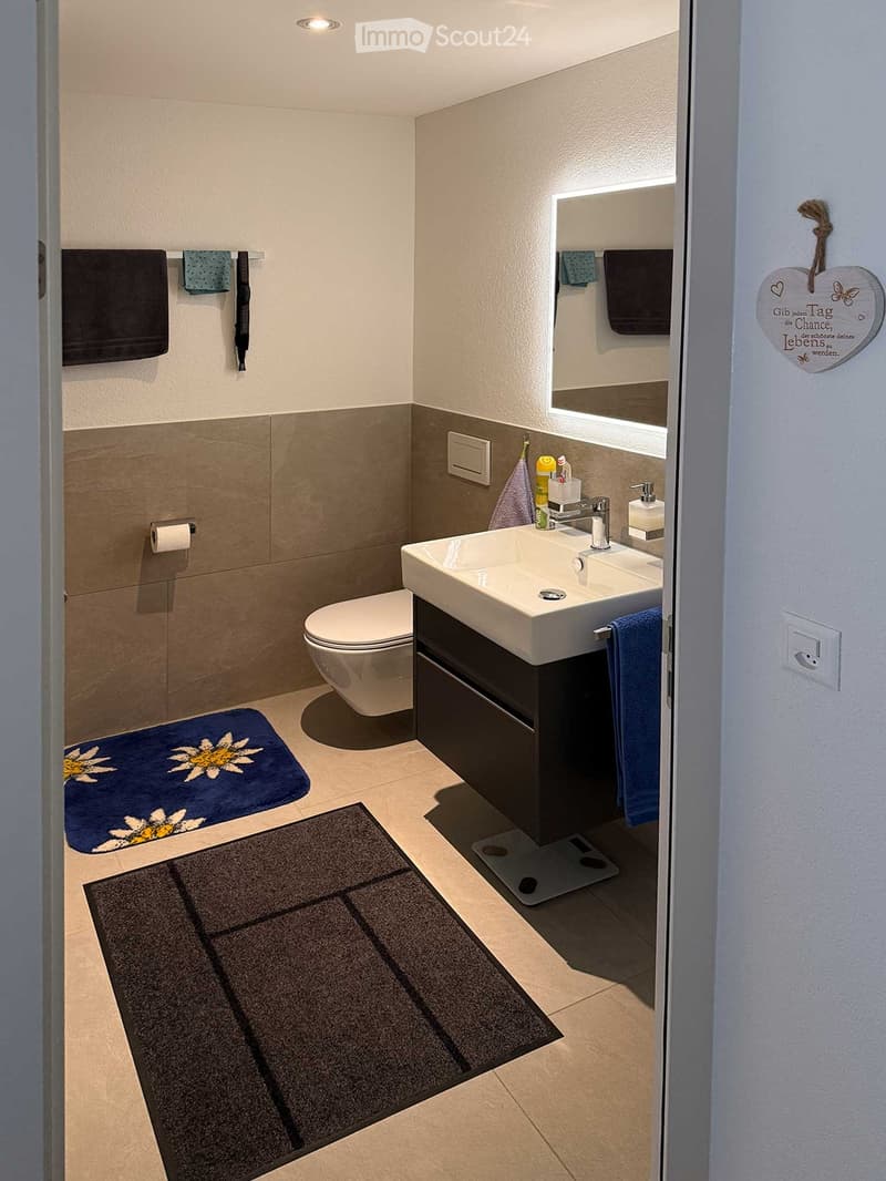 A modern bathroom with white fixtures, a walk-in shower, and towel rack. A sink is attached to a dark vanity and white floor. Towels are hanging on a bar, and a mirror reflects the room.