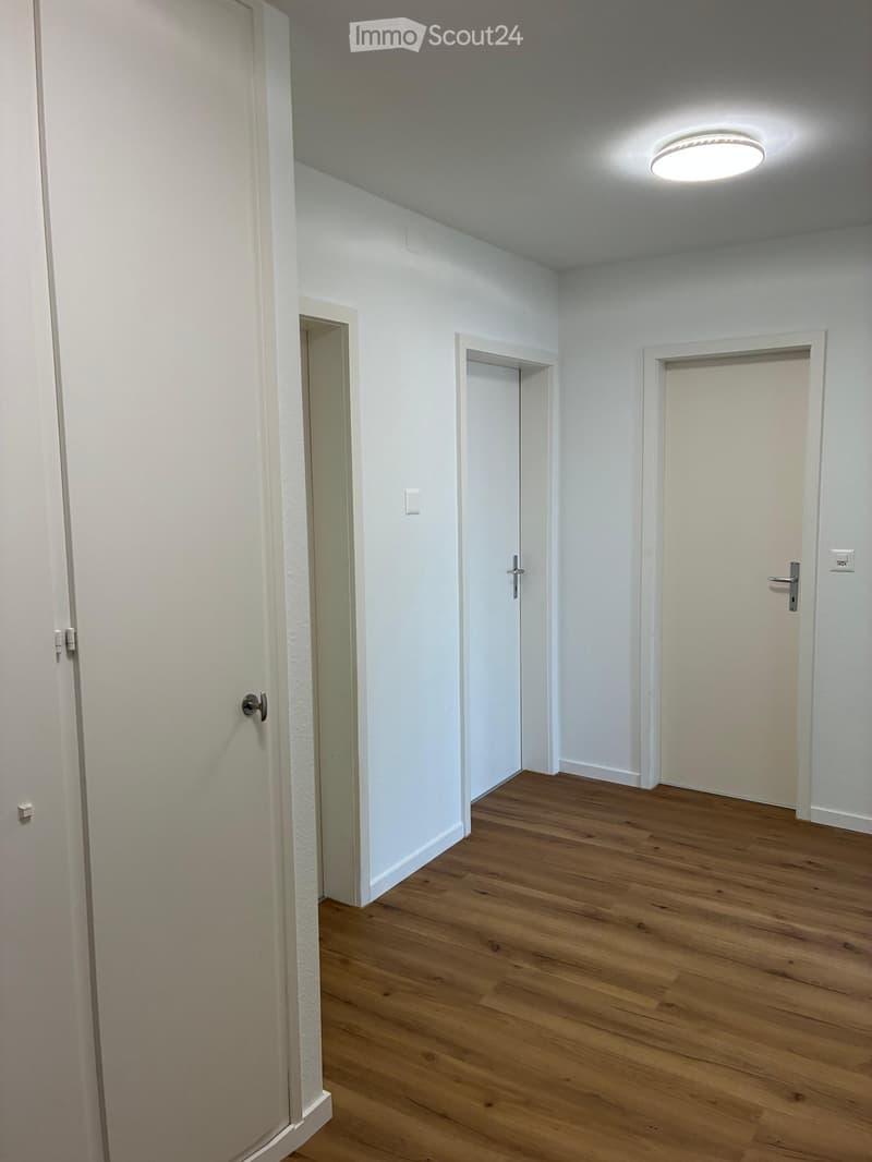 Empty hallway with wooden flooring, white walls, and several closed doors.