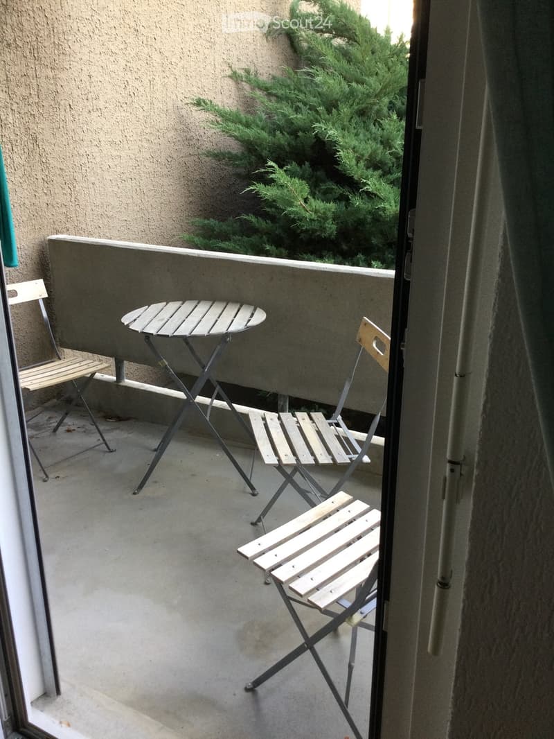 Balcony with a small round table and three wooden folding chairs, overlooking a green bush.
