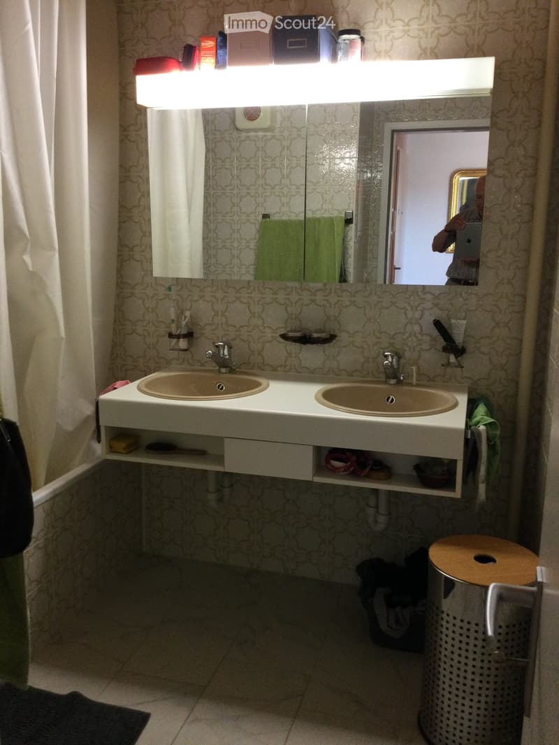 Bathroom with double sink, mirror, shelves, and various toiletries. Features patterned tiles and a built-in storage drawer.