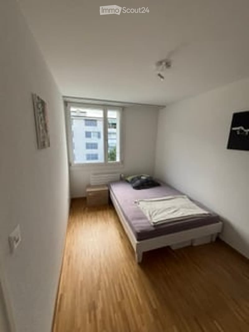 Small bedroom with wooden flooring, a single bed, a nightstand, and a window with blinds.