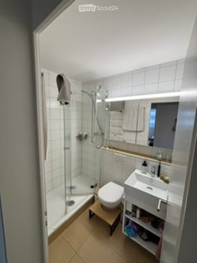 Modern bathroom with white tiled walls, a shower stall, a toilet, a sink with a mirror, and a towel hanging on the wall.
