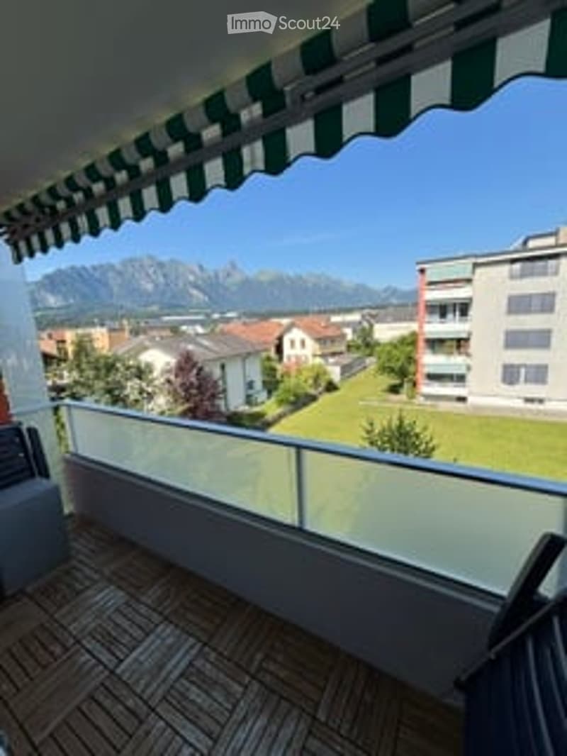 Balcony with wooden decking, glass railing, and scenic mountain view.