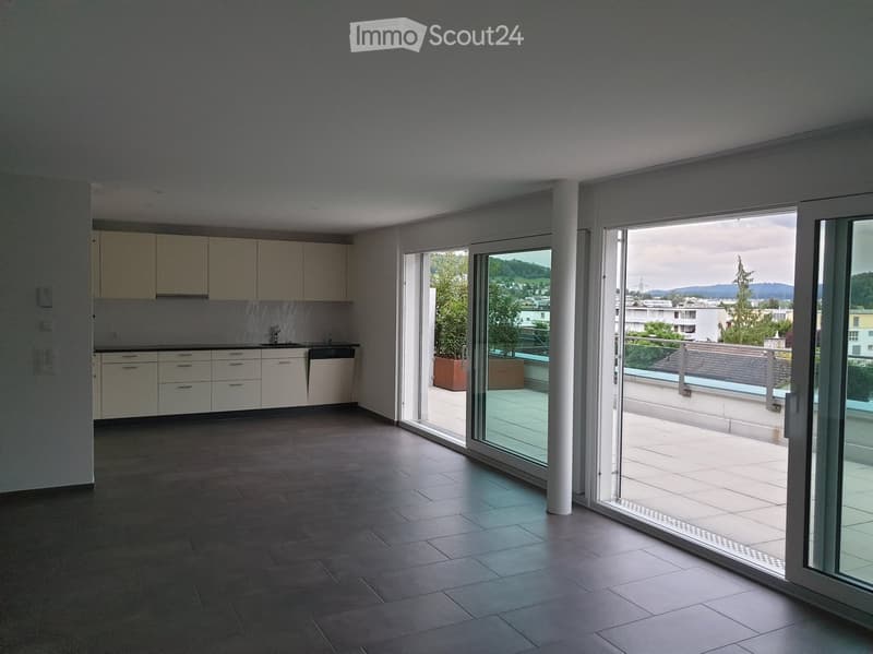 Modern kitchen with light-colored cabinets, a sink, and a dishwasher, connected to a spacious balcony with a view of the city and surrounding landscape.