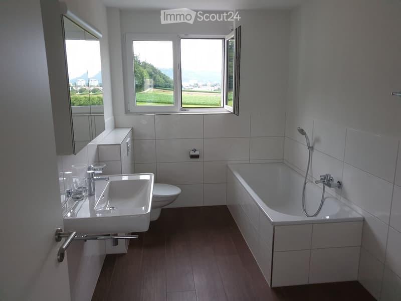 Modern bathroom with a white sink, bathtub, toilet, and large windows offering a scenic view.