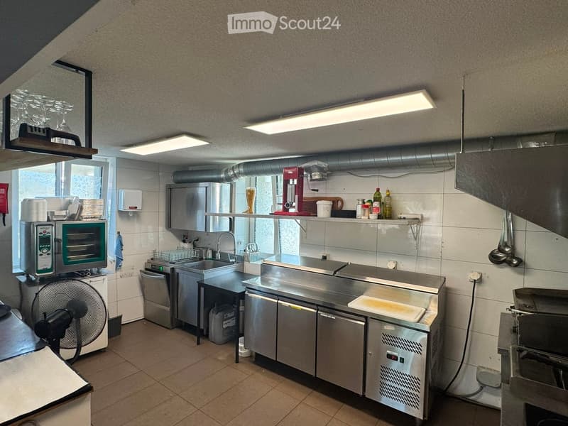Commercial kitchen with stainless steel appliances, microwave, oven, fridge, sink, and various utensils.