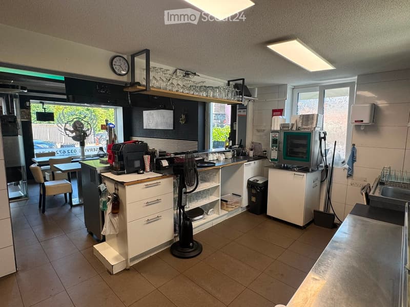 A modern kitchen with white cabinets, stainless steel appliances, a microwave, an oven, a fan, and a small dining area with a table and chairs.