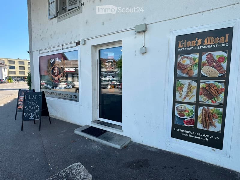Facade of "Lion's Meal" restaurant with large windows, signage, and menu board displaying food images and prices.
