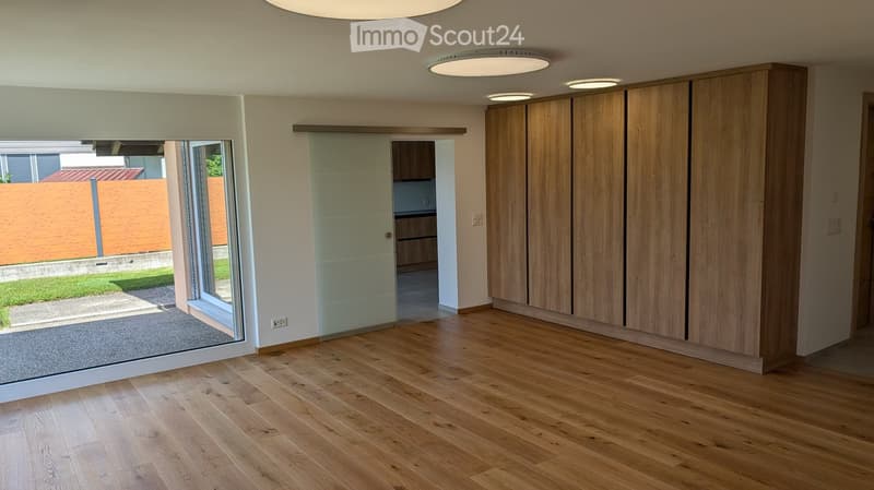 Empty room with wooden flooring, large glass sliding doors leading to an outdoor area, and built-in wooden cabinetry.