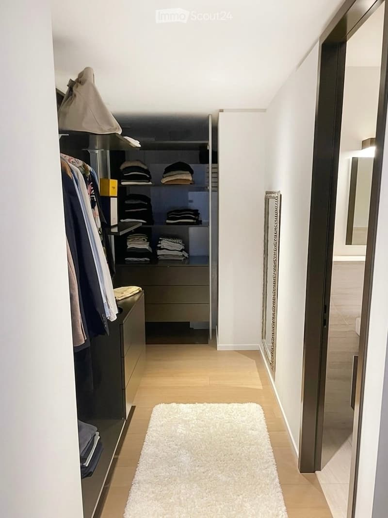 walk-in closet with wooden floor, white walls, built-in wardrobe, drawers, white rug, mirror