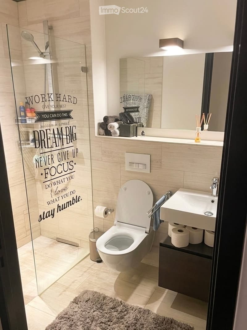 modern bathroom with glass shower, white sink, white toilet, wooden floor, motivational wall decals