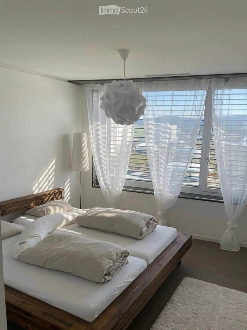 Double bed, white linens, pillows, white rug, white curtains, floor lamp, wooden ceiling lamp