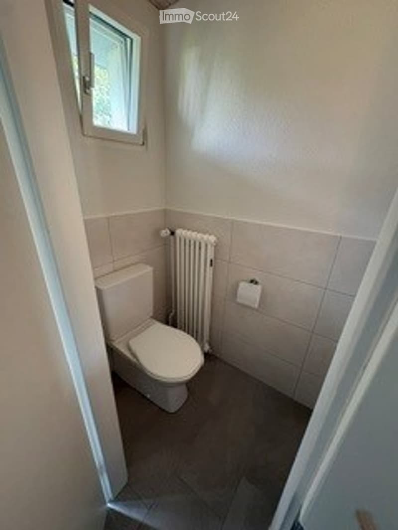 Small bathroom with white tiled walls, a toilet, a radiator, and a window allowing natural light.