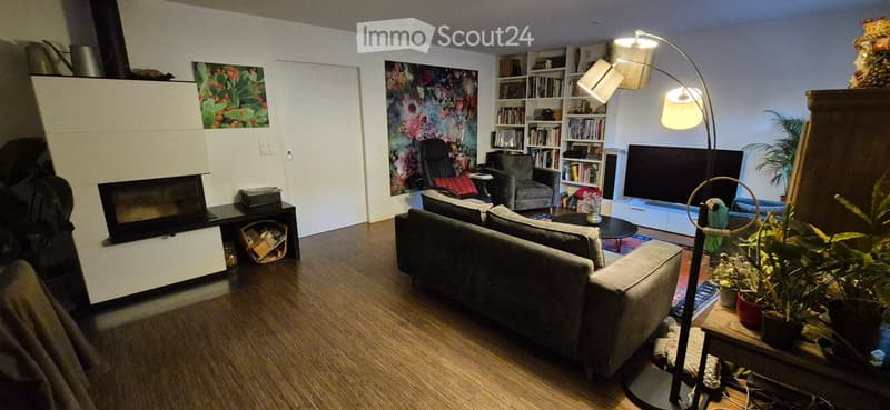 Modern living room with a grey sectional sofa, coffee table, armchair, bookshelf, floor lamp, television, and a fireplace.