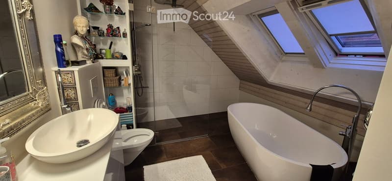 Modern bathroom with a freestanding bathtub, oval sink, toilet, glass-enclosed shower, and decorative shelves. Features skylights and a sleek design.