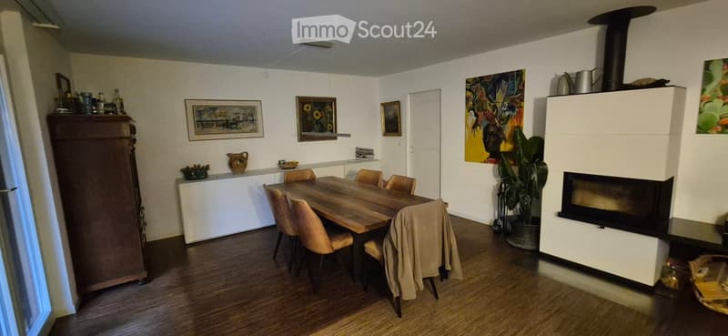 Dining room with a wooden dining table, six chairs, a cabinet, a fireplace, and several picture frames on the walls.