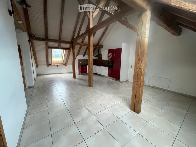 Open-plan space with exposed wooden beams, tiled floor, and a small kitchen area featuring red and white cabinets, an oven, and a range hood. A skylight provides natural light.