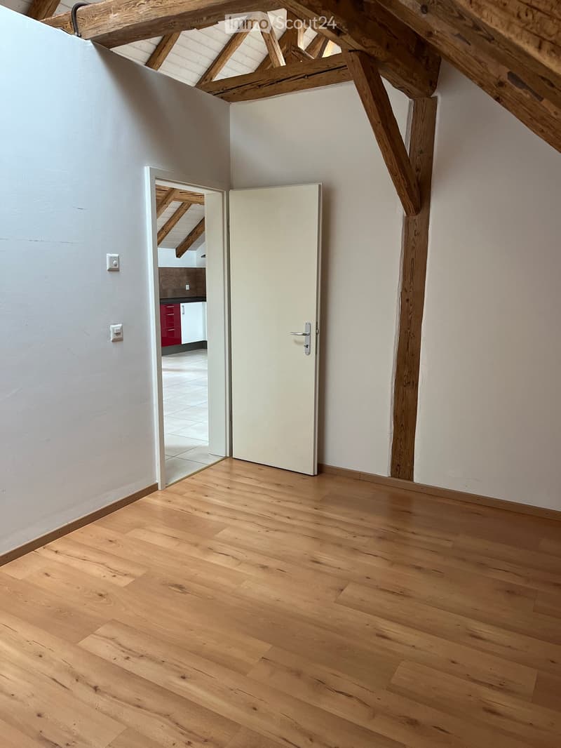 Empty room with wooden flooring, exposed wooden beams, and a white door leading to another room.
