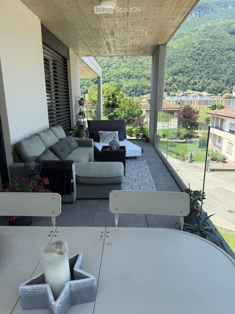 Modern balcony with a view, featuring a sofa, ottoman, chair, small table, and candle on a white table.