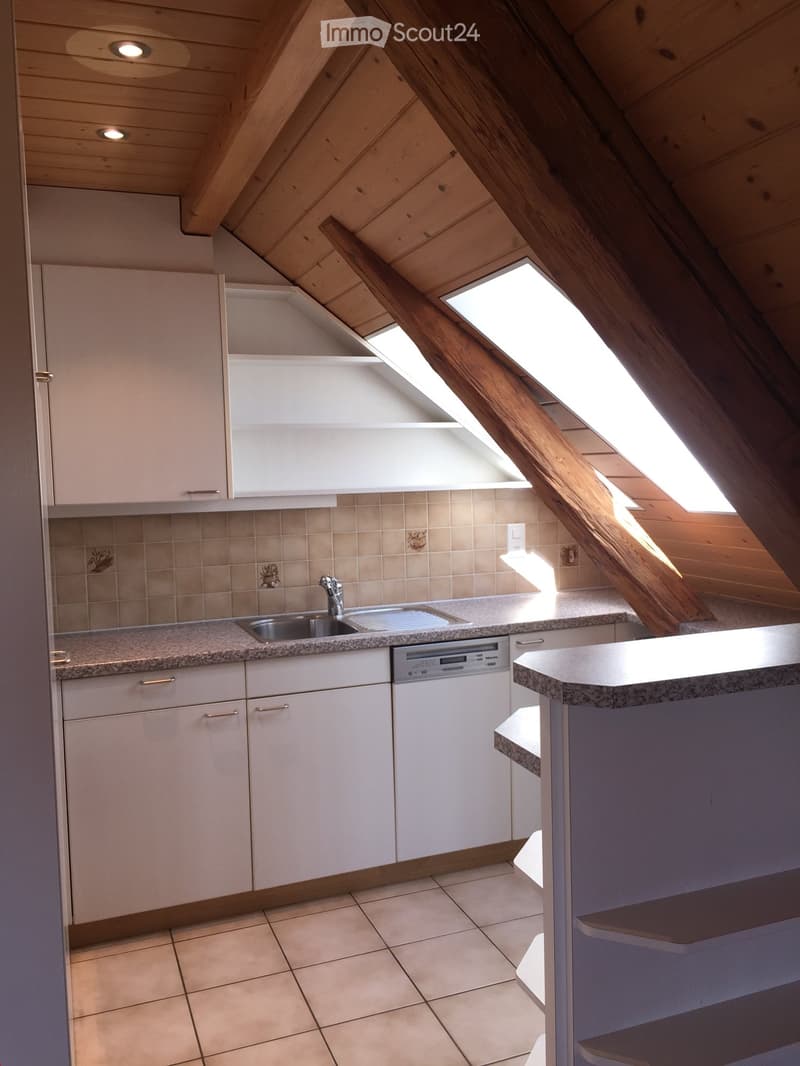 Modern kitchen with white cabinets, granite countertops, a sink, and a dishwasher, featuring skylight windows and wooden beams on the ceiling.