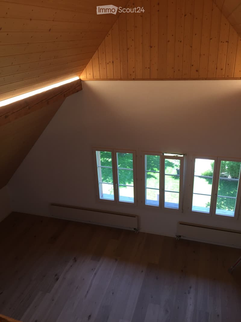 An empty attic room with wooden walls and ceiling, large windows, and wooden flooring.