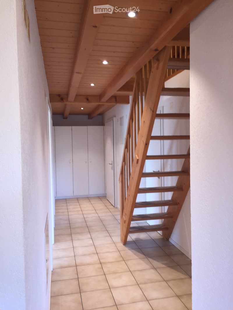 A modern hallway with a wooden staircase leading upwards, tiled floor, white walls, and built-in white cabinets on one side.