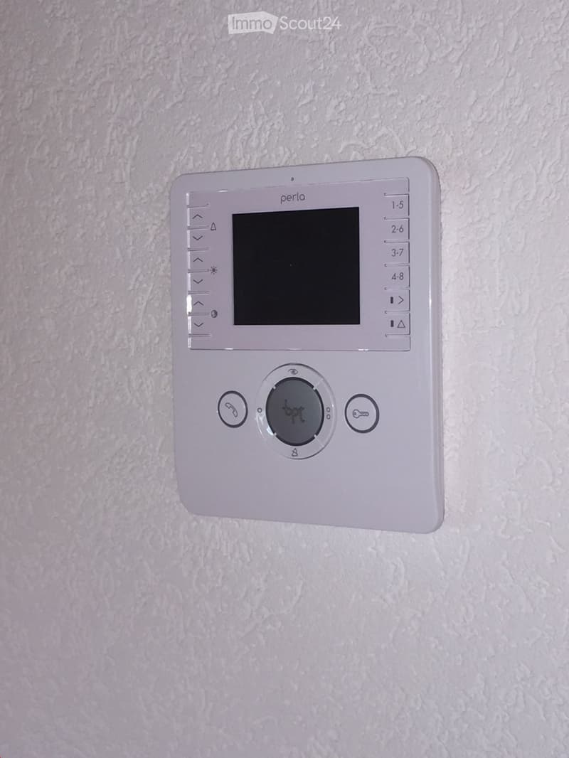A modern white thermostat with a digital display and multiple control buttons mounted on a textured wall.