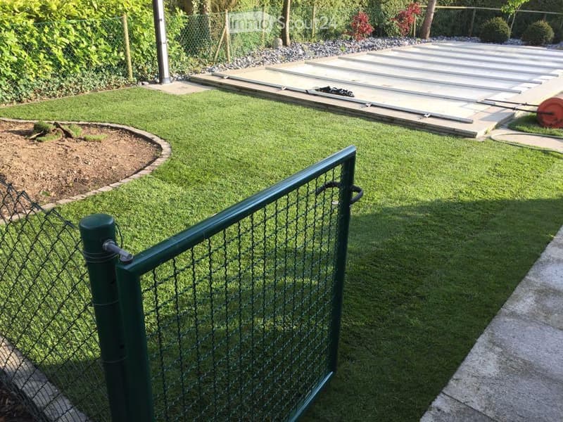 Well-maintained garden with artificial grass, a small raised bed, and a fenced perimeter. Includes a concrete pathway and a small storage area with tools.