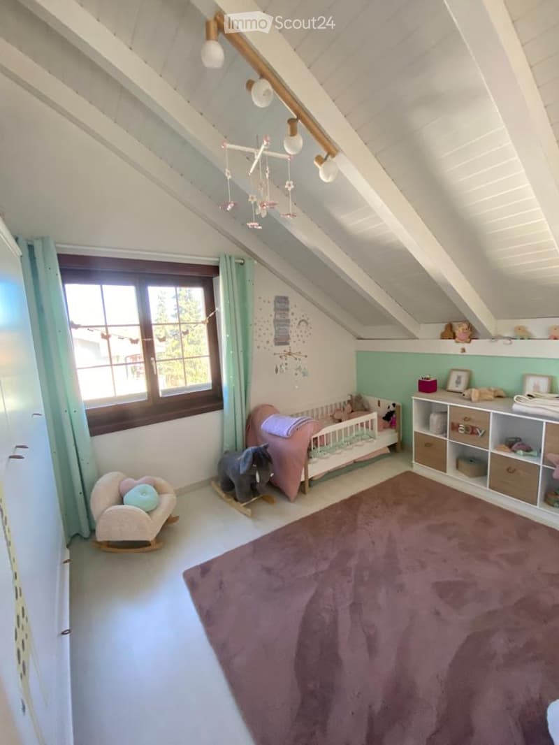 Cozy children's bedroom with slanted ceilings, a crib, rocking chair, toy elephant, shelf with storage boxes, and a large purple rug.
