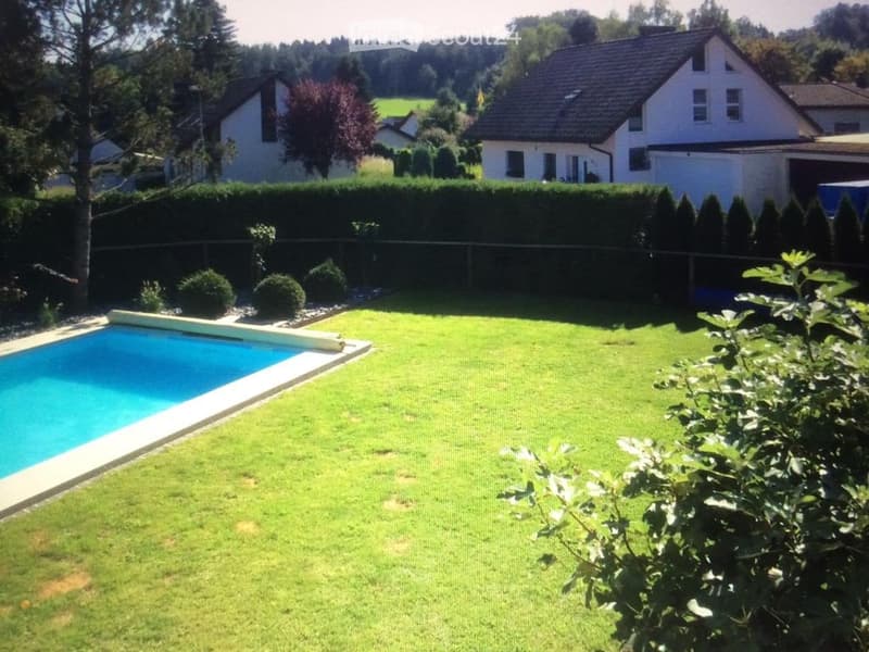 Well-maintained garden with a swimming pool, neatly trimmed hedges, and surrounding houses.