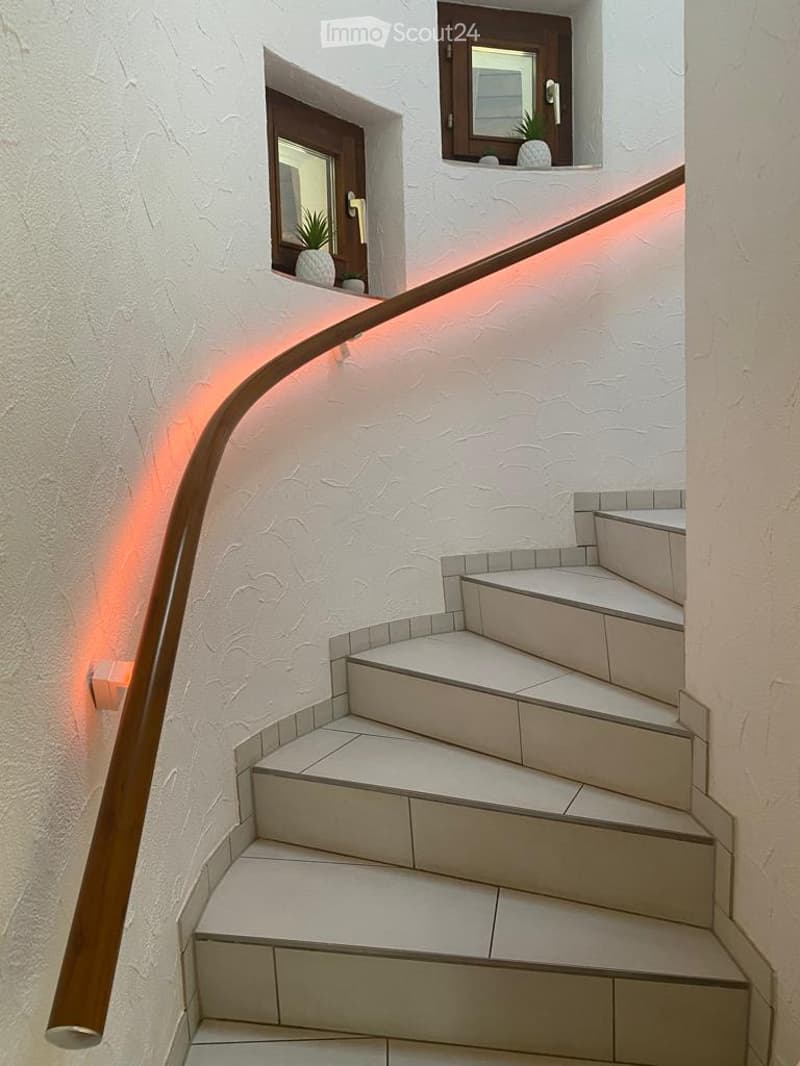 Spiral staircase with white tiled steps and a wooden handrail illuminated by warm lighting.