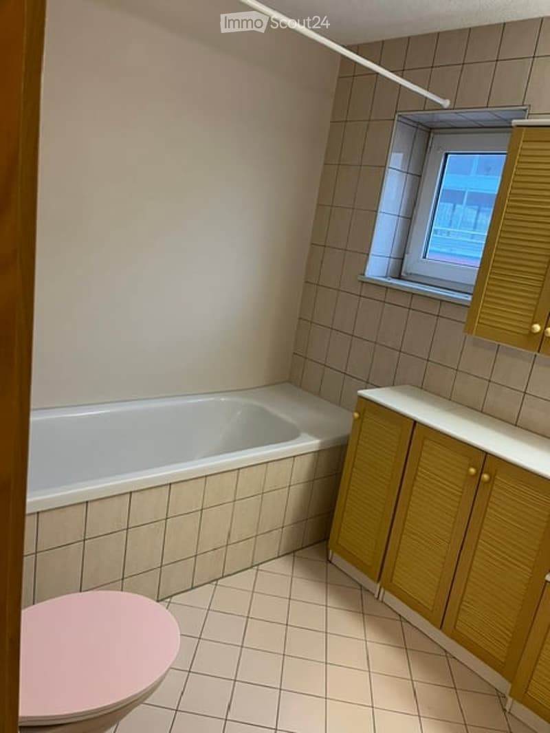 Bathroom with a white bathtub, pink toilet, and wooden cabinets.