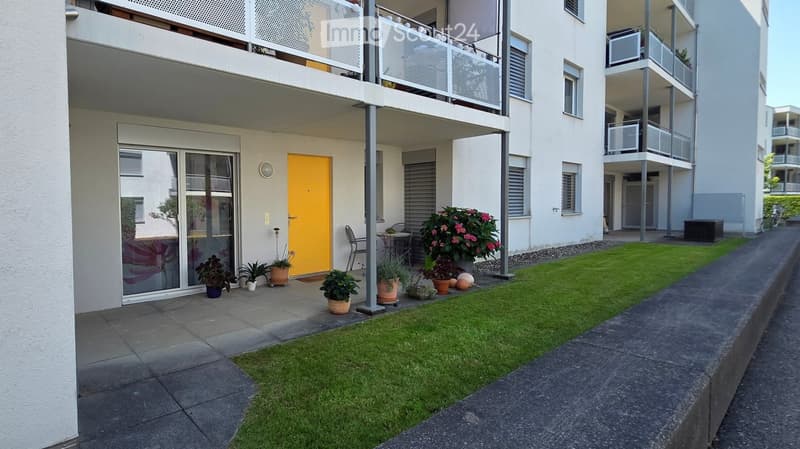 Balcony area with a small seating area, potted plants, and a view of the building.