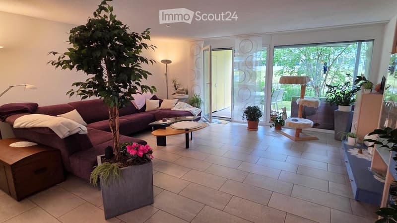 Modern living room with a red sectional sofa, coffee table, cat tree, floor lamp, and large potted plant near the sliding glass doors leading to a garden.