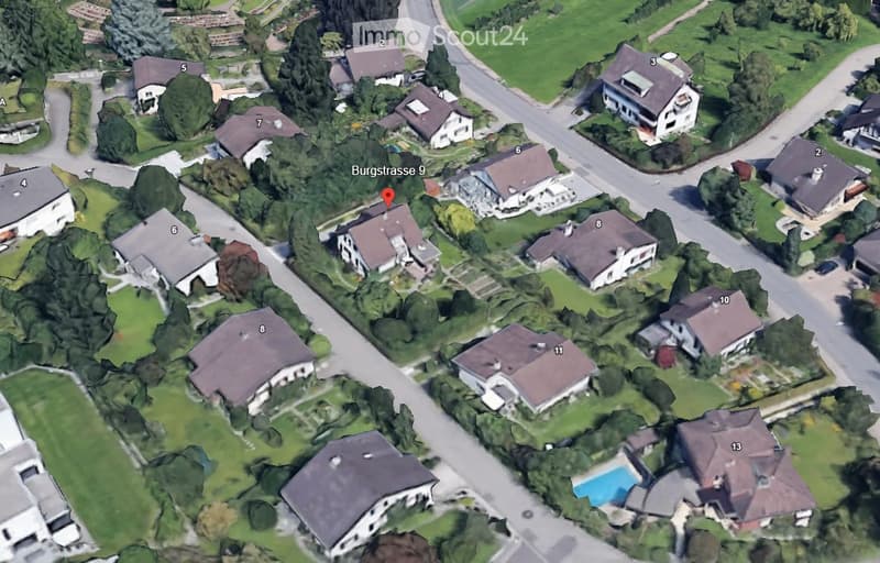 Aerial view of a residential neighborhood with multiple houses, gardens, and a swimming pool visible in the lower right area.