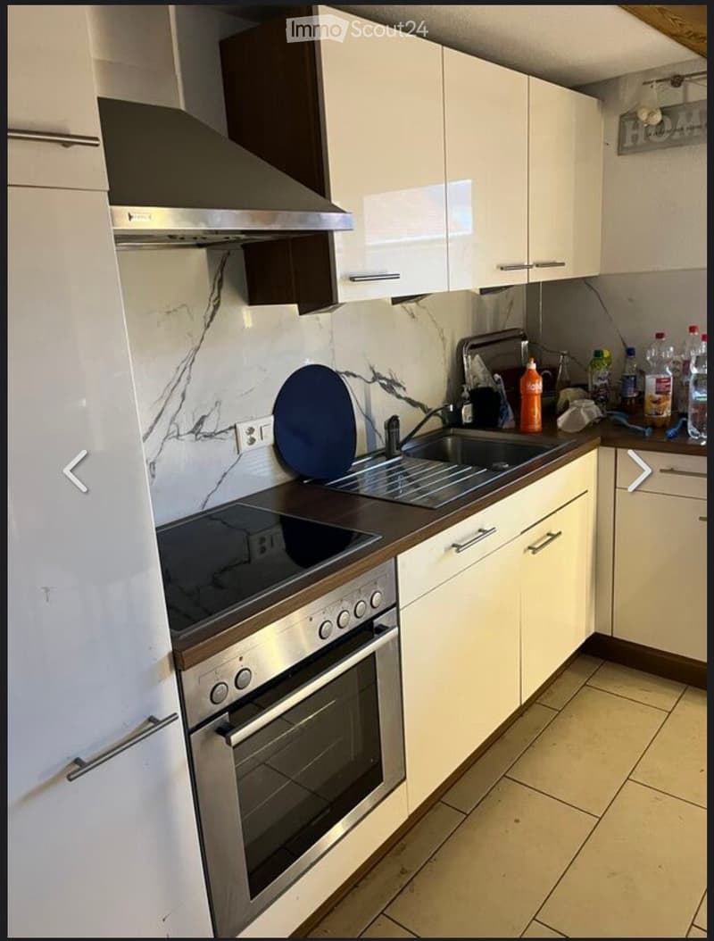 Modern kitchen with white cabinets, stainless steel appliances, marble backsplash, and a countertop with various items.