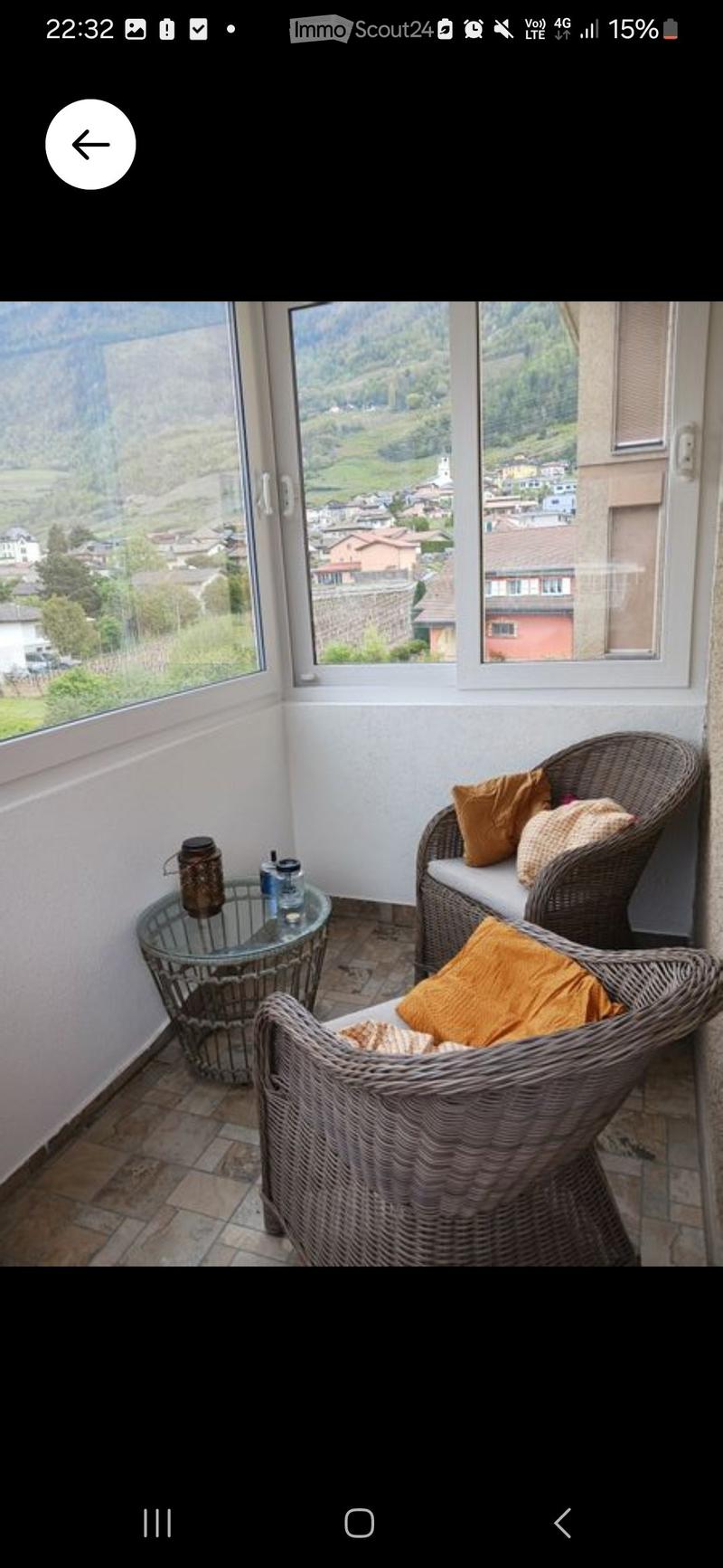 Balcony with wicker seating, glass table, and scenic mountain view.