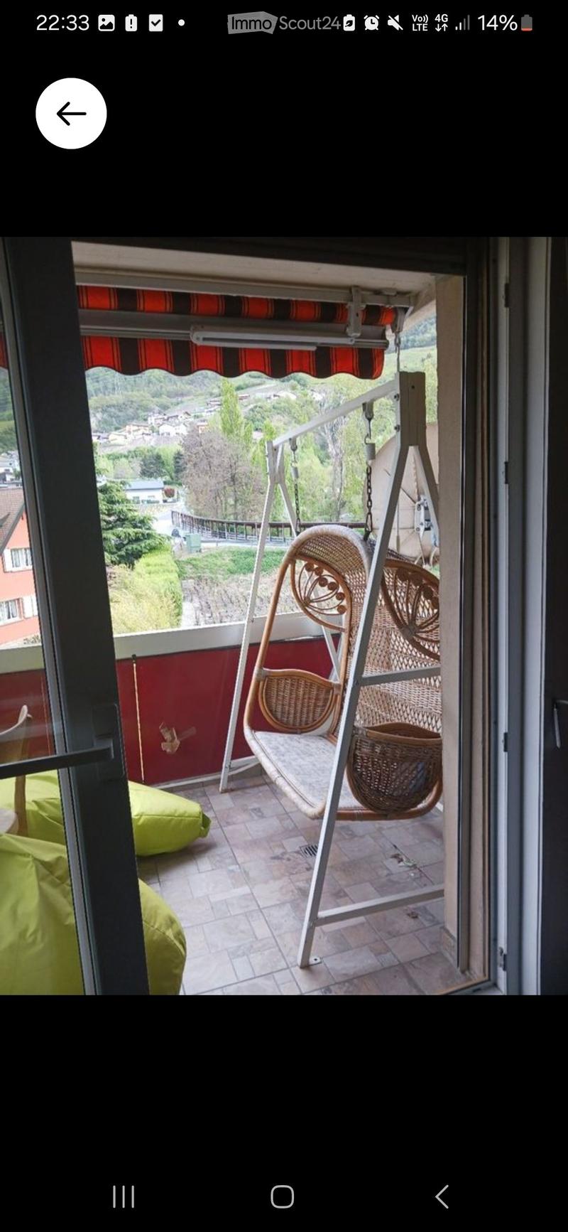 Balcony with tiled floor, red wall, wicker swing chair, and green cushions visible through an open doorway.