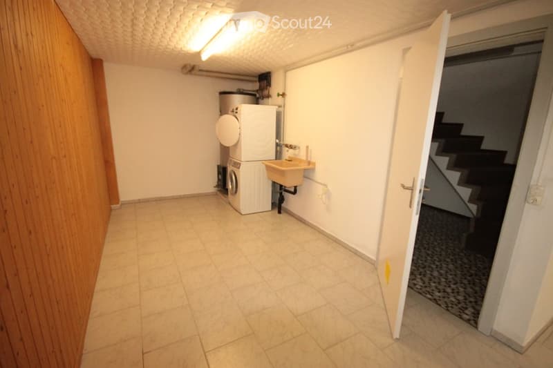 Empty laundry room with tiled floor, white walls, a washing machine, and a small sink. A staircase leads upwards.