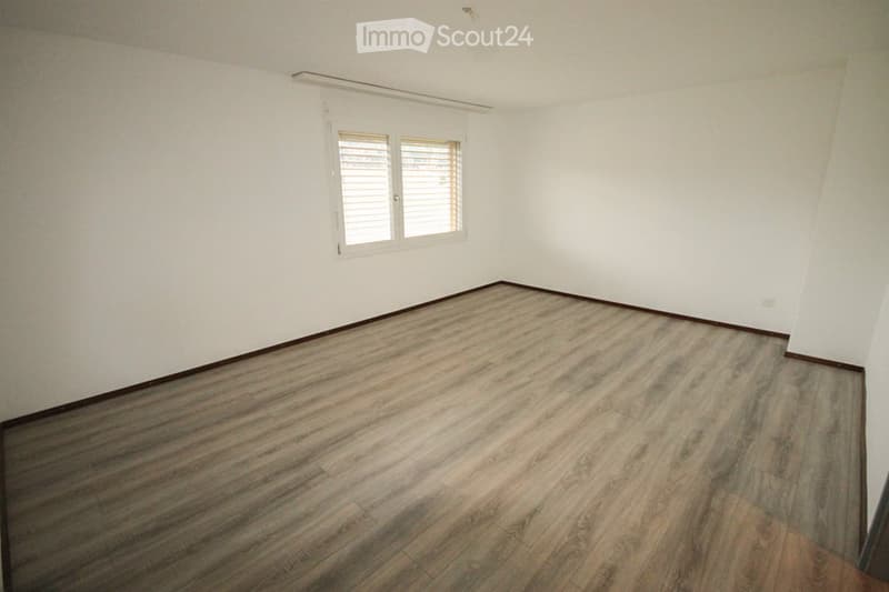 Empty room with white walls, wooden flooring, and a single window with blinds.