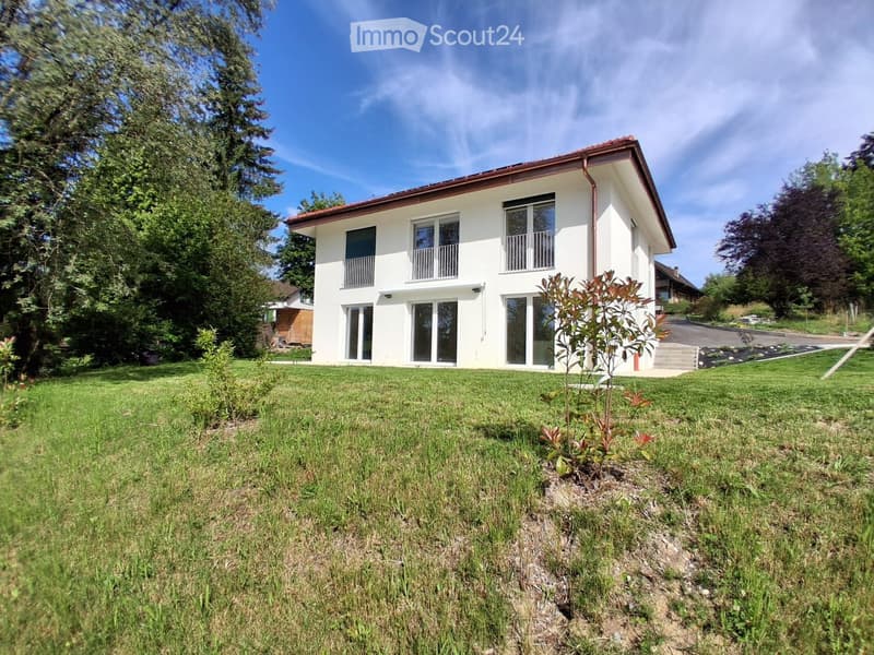 Two-story white house with large windows and balconies, surrounded by a well-maintained lawn and trees.