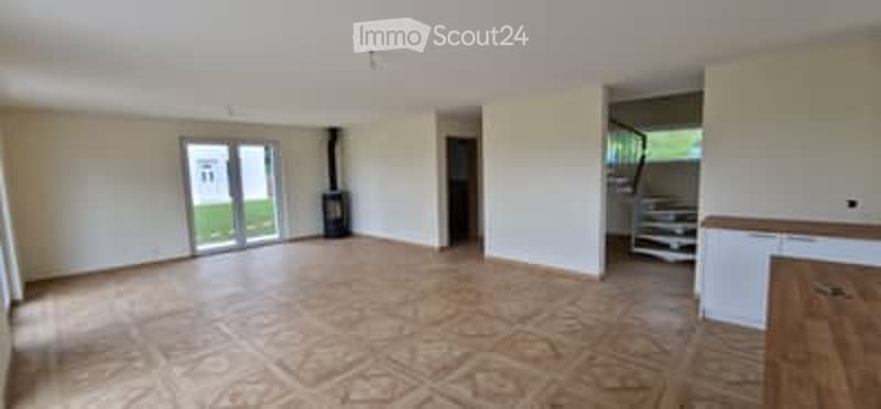 Empty room with wooden flooring, large glass door leading to outdoor area, white walls, and a visible staircase in the background.