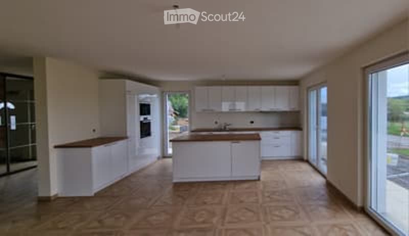 Modern kitchen with white cabinets, a central island, and large windows. The floor is tiled in a warm wood pattern.