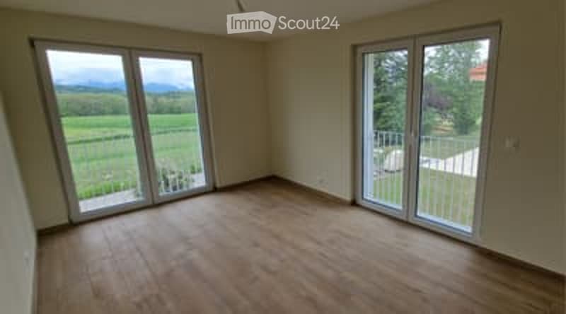 Empty room with wooden flooring, large sliding glass doors leading to a balcony, and a view of a green field.