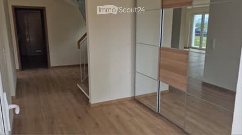 A modern hallway with wooden flooring, white walls, a large mirrored closet, and a staircase leading upwards.